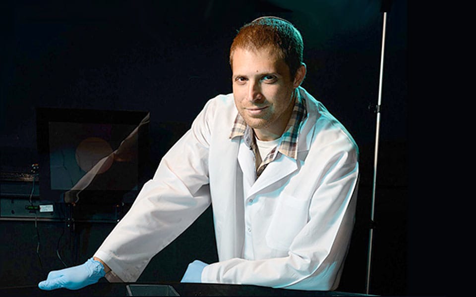 Scientist wearing a lab coat and gloves, posing in a laboratory setting with equipment in the background, showcasing a professional research environment.