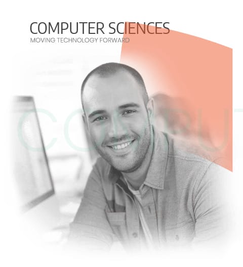 Smiling man in a casual shirt working at a computer, representing the field of computer sciences and technology advancement.