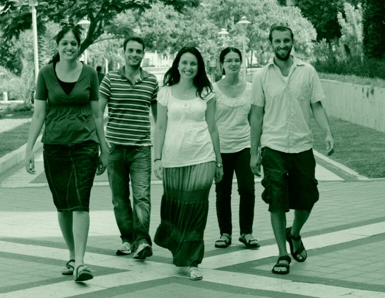 Five young adults, three women and two men, walk together on a paved path.