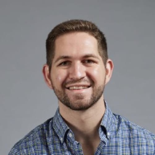 Headshot of a man with short brown hair and a beard, wearing a blue and white plaid shirt.