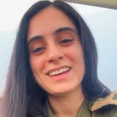 Close-up of a smiling young woman with long dark hair, wearing a military-style jacket.